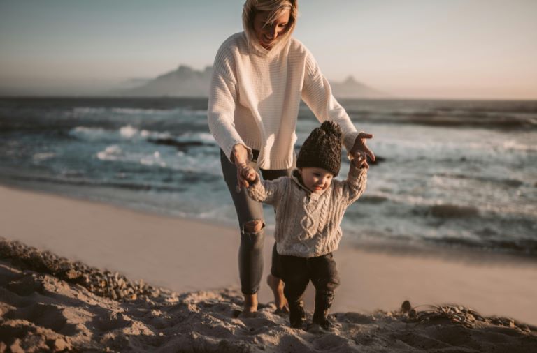 Une maman marche sur la plage avec son bébé. Elle a l'air épanouie car elle connait la théorie de l'attachement, cette théorie que tous les parents devraient connaitre