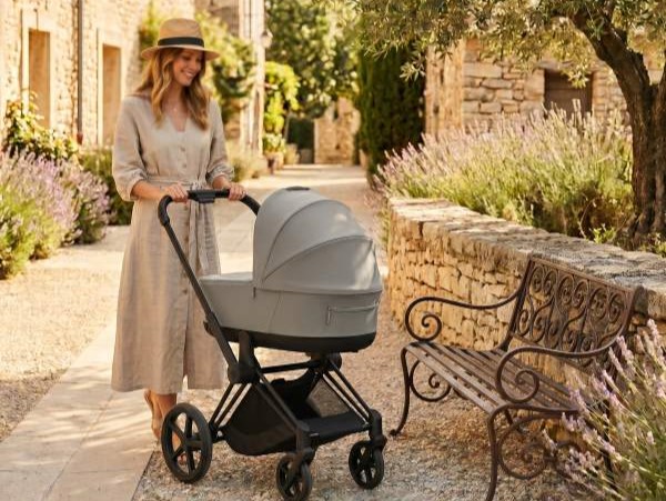 poussette 3 en 1 moderne avec nacelle, maman se promenant dans un village provençal ensoleillé avec allée en gravier et banc en fer forgé