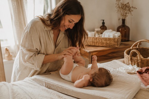 Maman changeant son bébé sur un lit dans une chambre lumineuse, illustration d’un abonnement couches pratique pour simplifier le quotidien des jeunes parents.