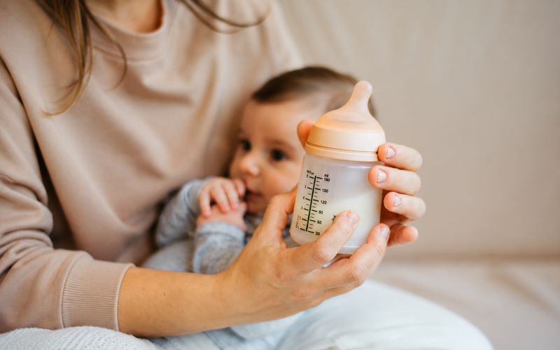 Reprise du travail et allaitement : maman proposant un biberon de lait maternel à son bébé avant le retour au travail