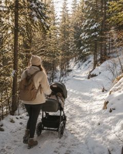 Comment habiller bébé au ski : maman se baladant avec bébé en poussette tout-terrain sur un chemin enneigé au milieu des sapins en montagne.
