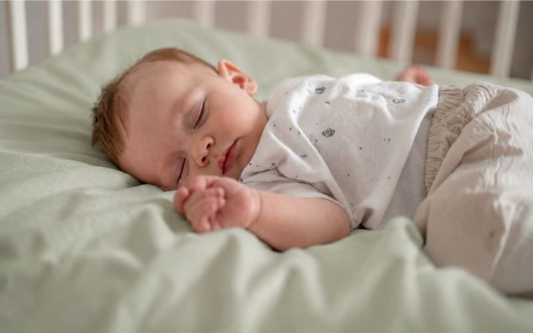 Routine du soir bébé : bébé endormi paisiblement dans son lit sur un drap-housse vert sauge après le rituel du coucher.